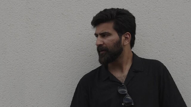 Moody portrait of a bearded man smoking a cigarette against a white wall
