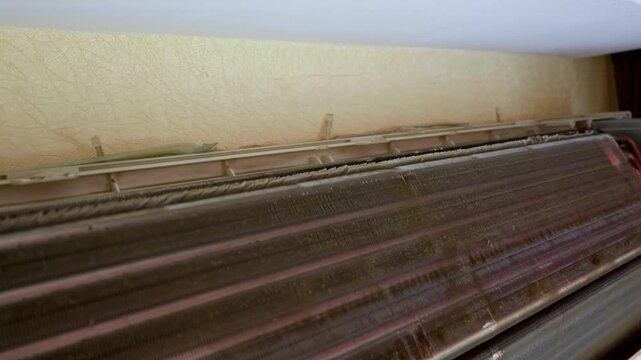 Close-up of a disassembled wall-mounted air conditioner showing dirty fins clogged with hazardous mold and black dust. Concept of indoor air pollution, allergen risks, and HVAC maintenance.