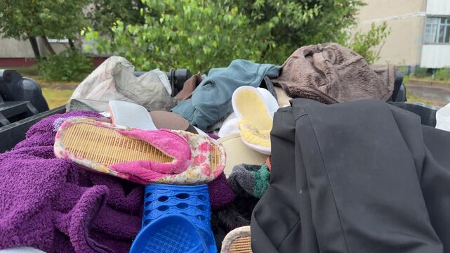 Discarded clothing shoes and household items in a waste container outdoors. trash garbage disposal purple towels slippers fabrics urban waste collection