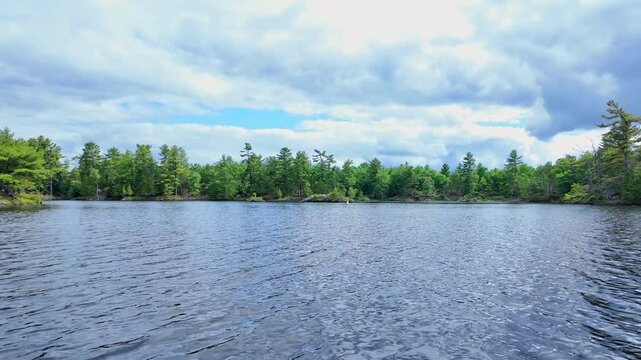 POV boat in motion, the view across open water toward a rugged, tree-covered shore. Soft wind ripples water surface, creating a peaceful, natural scene ideal for a serene movie background shot.
