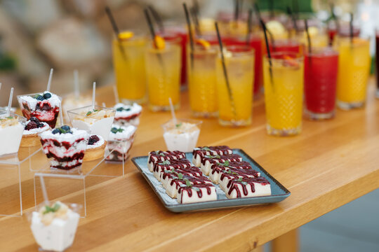 Catering buffet table with sweet mini desserts in cups and refreshing cocktails.
