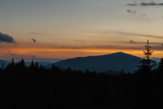 Beautiful evening twilight with bright orange sky above dark mountain ridges.