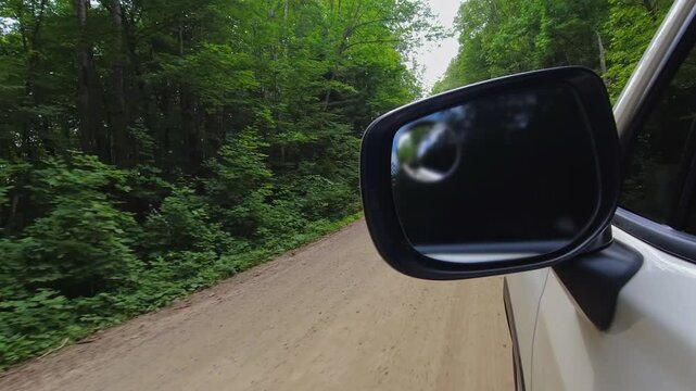 Frame with cars side mirror during the travel on the cottage country rural road in North America. Half view of side rear view mirror of a car driving along the highway, and half of road and nature.