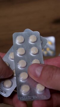 Male hands hold two silver blister packs of round yellow medicine tablets over a wooden table. Concept of healthcare treatment, pharmacy prescription medication, and daily vitamin supplements.