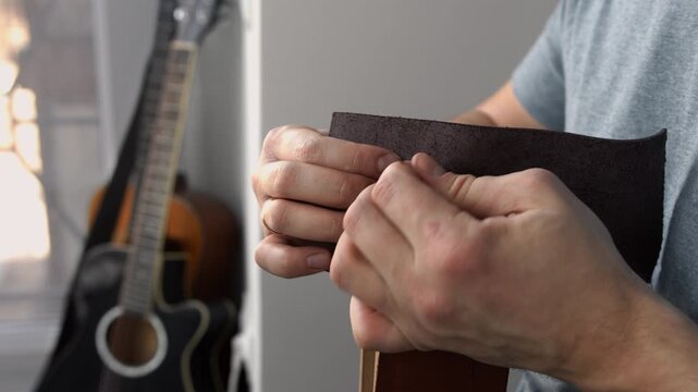 Artisan craftsman sewing brown genuine leather with needle and thread creating a handmade accessory in a workshop