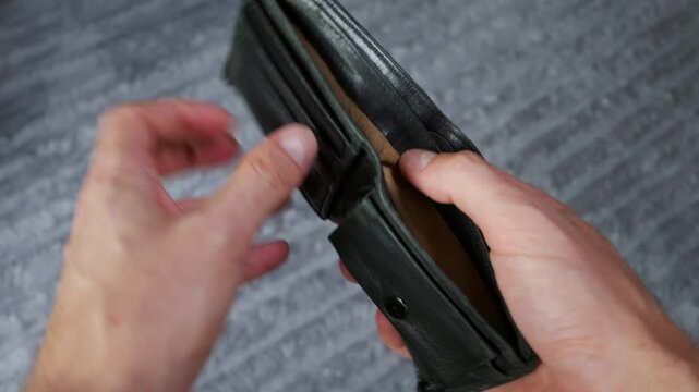 Hands hold open a completely empty black leather wallet showing no cash or credit cards inside. Concept of financial crisis, poverty, personal bankruptcy, debt, and inflation.