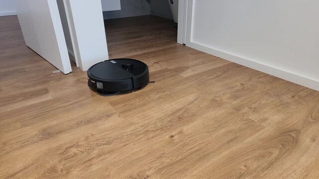 Autonomous robot vacuum moving across laminate flooring inside a bright modern apartment. Smart cleaning appliance maintaining tidy floors with automatic navigation.