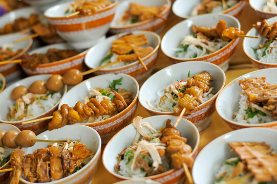 Close up of Indonesian soto ingredients served dry before broth, rice bowls with satay skewers, shredded chicken and herbs. Traditional street food presentation.