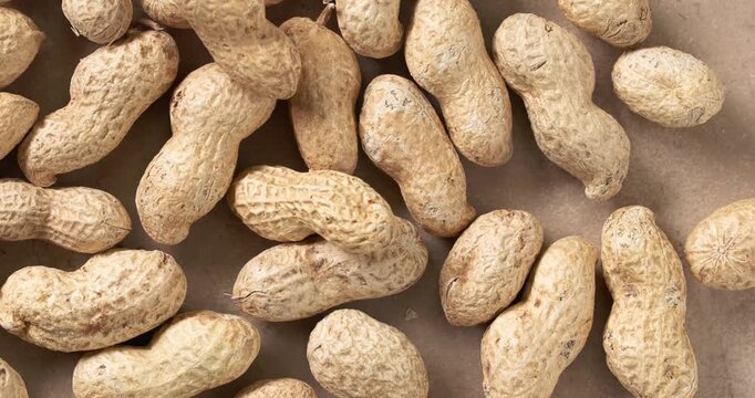 unshelled peanuts rotating on a rustic kitchen tabletop. Natural whole peanuts in shells arranged in a scattered composition, showcasing organic texture and freshness. Premium 4K food video
