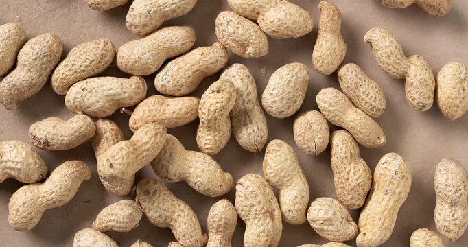 unshelled peanuts rotating on a rustic kitchen tabletop. Natural whole peanuts in shells arranged in a scattered composition, showcasing organic texture and freshness. Premium 4K food video