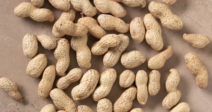 unshelled peanuts rotating on a rustic kitchen tabletop. Natural whole peanuts in shells arranged in a scattered composition, showcasing organic texture and freshness. Premium 4K food video