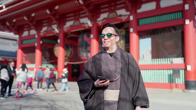 Young smiling Latino man feeling happy, curious and relaxed using his smartphone at Sensoji Temple in Asakusa Tokyo Japan, iconic historic site, traditional architecture, wearing kimono and sunglasses