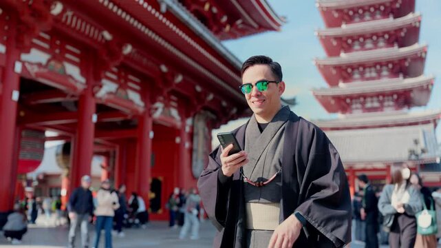 Young smiling Latino man feeling happy, curious and relaxed using his smartphone at Sensoji Temple in Asakusa Tokyo Japan, iconic historic site, traditional architecture, wearing kimono and sunglasses