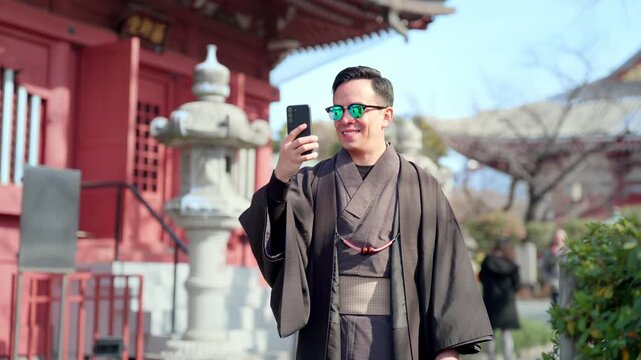 Young smiling Latino man feeling happy, curious and relaxed using his smartphone at Sensoji Temple in Asakusa Tokyo Japan, iconic historic site, traditional architecture, wearing kimono and sunglasses