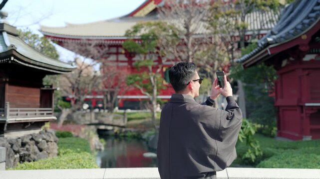 Unrecognized young smiling Latino man calm, curious while taking a photo with his smartphone at Sensoji Temple in Asakusa Tokyo Japan, iconic historic landmark with pagoda, wearing traditional kimono