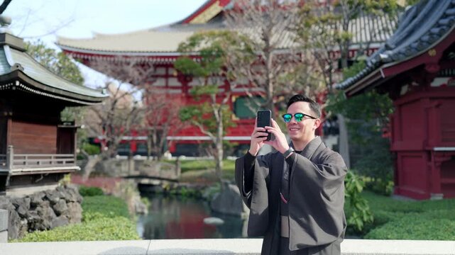 Young smiling Latino man feeling happy, curious and relaxed using his smartphone at Sensoji Temple in Asakusa Tokyo Japan, iconic historic site, traditional architecture, wearing kimono and sunglasses