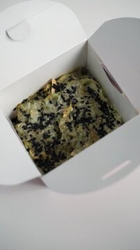 White takeout box opening to reveal a fresh Korean bindae-tteok pancake isolated on a white background