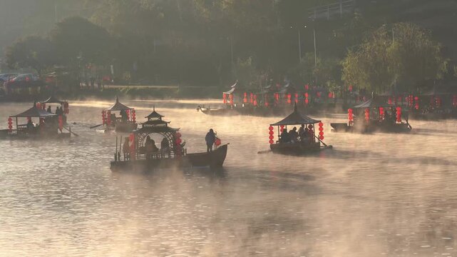 Rak Thai Village, Mae Hong Son, Thailand - November 25, 2025: Traditional Chinese-style boats sail on a misty lake during a beautiful winter at Ban Rak Thai village. Famous travel destination.