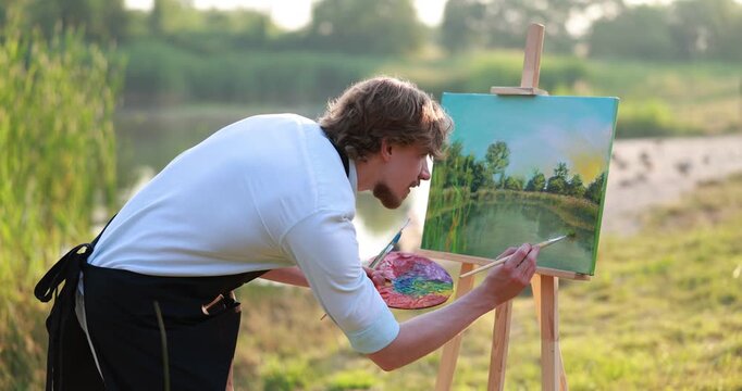 Man painting beautiful landscape on canvas. Artist working outdoors