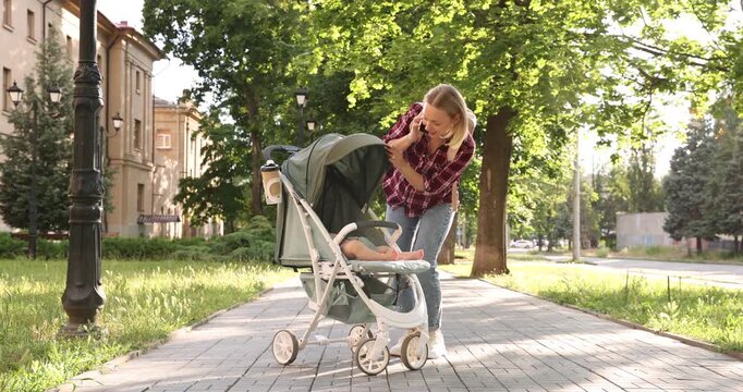 Baby carriage. Mother talking on smartphone while walking with her child in stroller outdoors