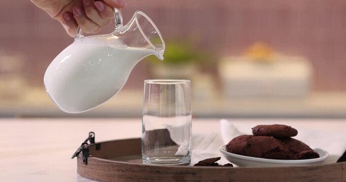 Woman pouring fresh milk into glass at table in kitchen, closeup. Camera moving