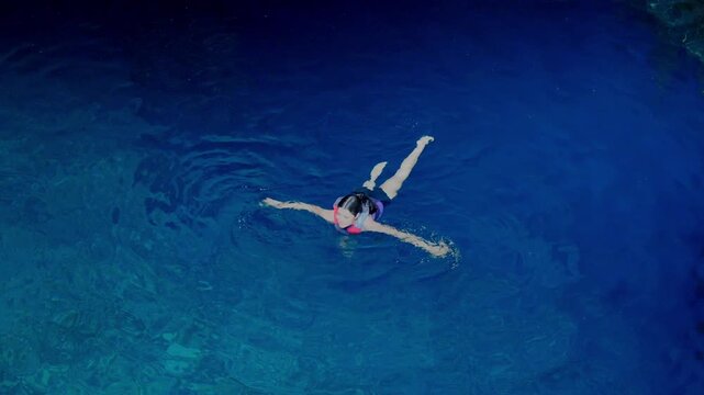 Young smiling Latina woman relaxed and adventurous while floating and swimming in a deep blue cenote in Yucatan Mexico, surrounded by clear freshwater and rocky walls, wearing life jacket and swimwear