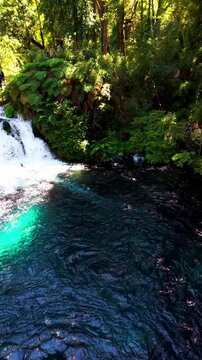 Aerial vertical tracking shot panning over a roaring waterfall flowing into a crystal clear turquoise pool