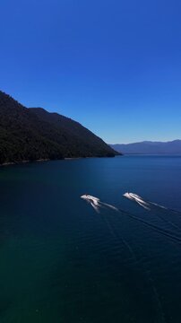 Aerial vertical tracking shot following three jet skis racing across a calm blue lake on a sunny day