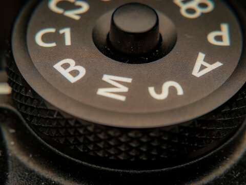 Macro extreme close-up of a black camera mode dial showing exposure settings like manual, aperture, and shutter priority
