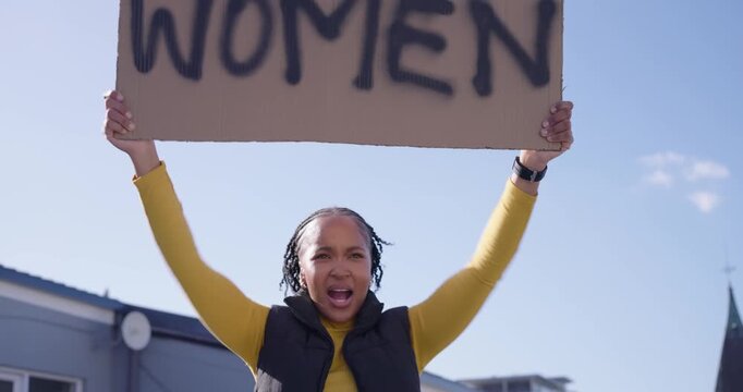 Woman walking onto rooftop in yellow top and black vest, carrying WOMEN placard, protesting loudly