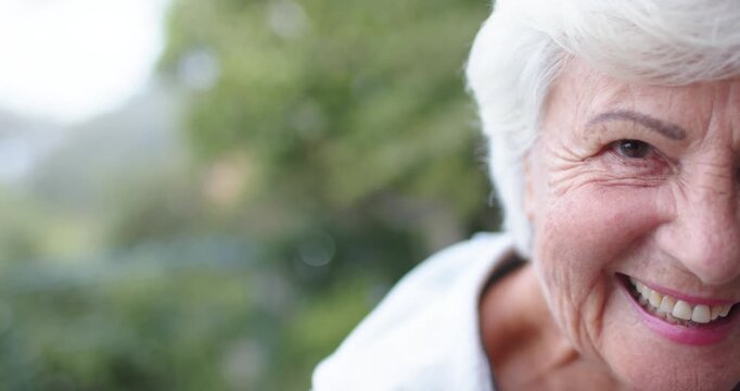 Senior woman entering right leaning to camera smiling pale top balcony foliage railing, copy space