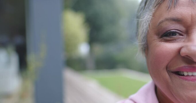 Senior African American woman hearing voice smiling leaning laughing on porch post, copy space