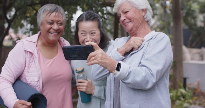 Diverse women leaning in laughing senior woman holding phone guiding, center bottle, left mat park