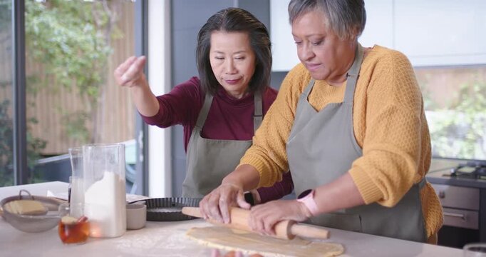 Diverse women placing dough, rolling pastry and dusting flour at island for tart with rolling pin