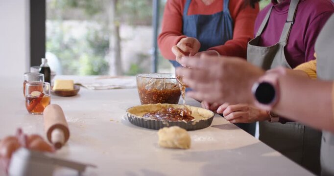 Diverse women in aprons spoon scooping, assembling tart at counter, spooning into crust to bake