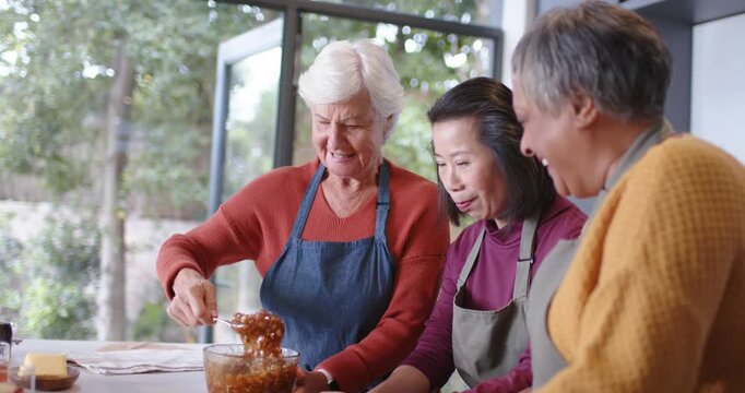 Diverse female friends in aprons gathering in kitchen, preparing pie, scooping filling into crust