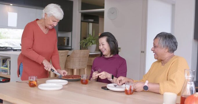Diverse women with senior starting slicing pie at dining table, serving plates and preparing to eat