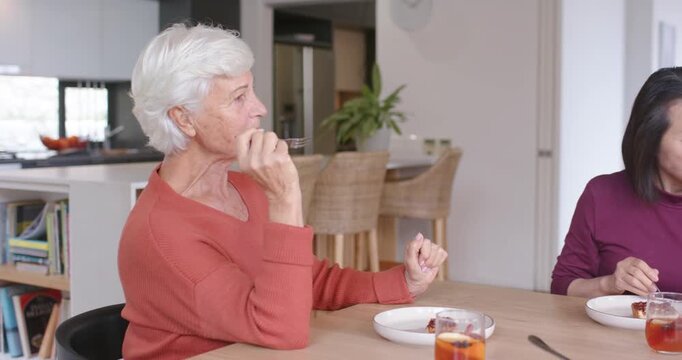 Senior woman and Asian woman prompted by pecan pie lifting forks, cutting, tasting dessert at home