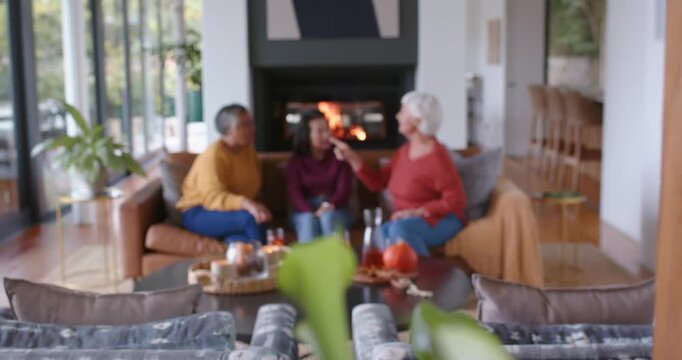 Diverse female friends reacting after senior woman offering small item by fireplace coffee table