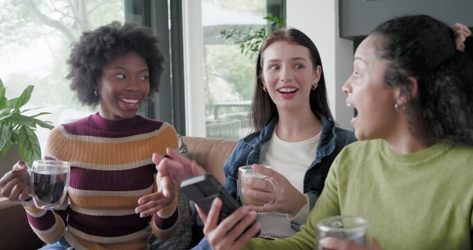 Diverse female friends reacting to playback singing high-fiving, passing device on sofa with mugs