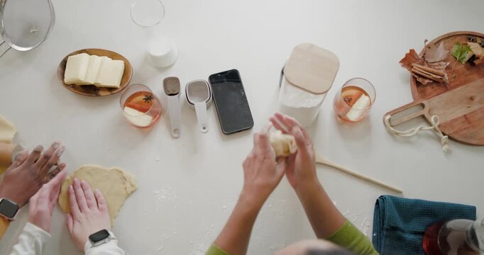 Female friends starting baking session rolling and pressing dough on counter with rolling pin