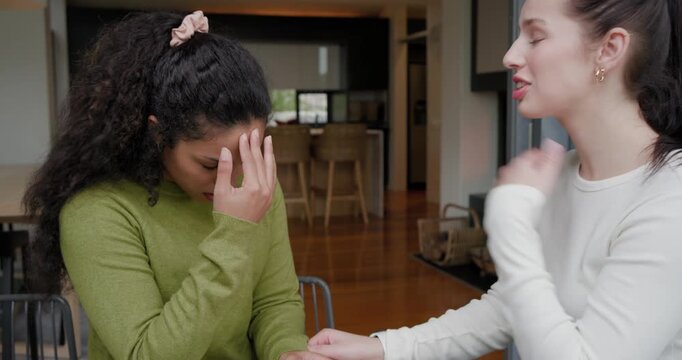Diverse female friends at wood table, woman in white reaching, holding hands, comforting friend