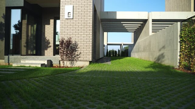 Concrete beams casting moving shadows on a green turf block paver driveway in a modern architectural building's courtyard under a clear sunny sky creating a dynamic pattern