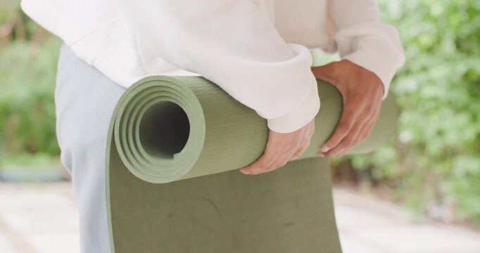 African American woman in white top, pants adjusting green yoga mat on patio, preparing for yoga