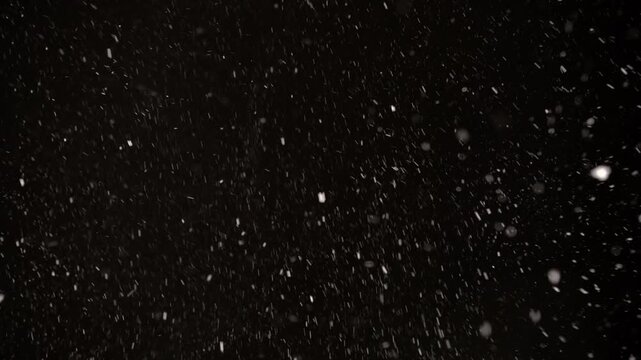 Snowflakes swirl and cascade in a vibrant winter storm, creating a breathtaking contrast against the deep black sky. Nature's beauty unfolds in every flake