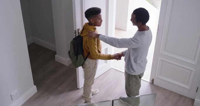 African American father-son starting goodbye shake patting son leaving foyer with backpack