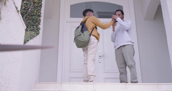 African American male teen arriving on porch greeting dad giving phone fixing backpack fist bumping