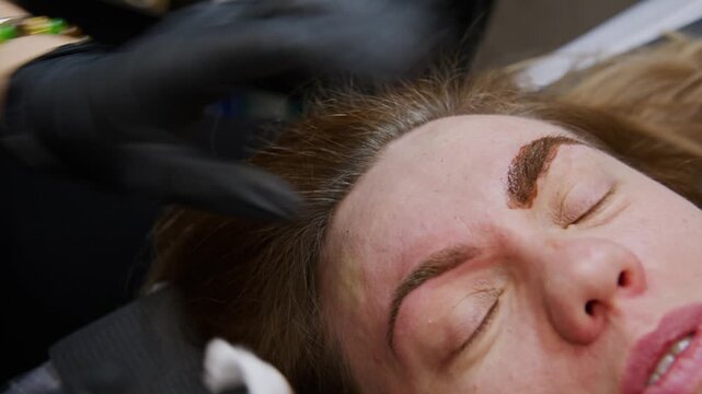 Witness the skillful application of eyebrow tattooing as a professional beautician uses a specialized tool. Close-up shots show the intricate process, ensuring perfect brow definition and enhancement