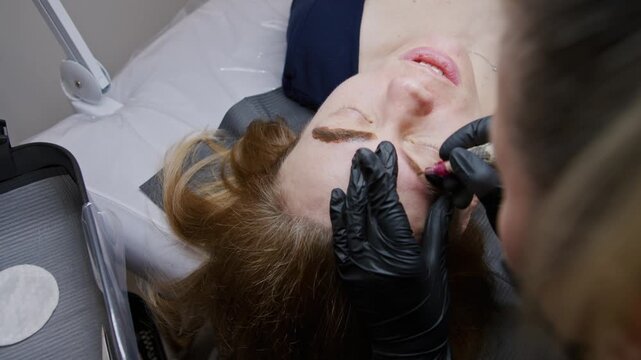 Watch as a skilled beautician performs eyebrow tattooing using a specialized machine. The process involves precise application of pigment for a stunning transformation
