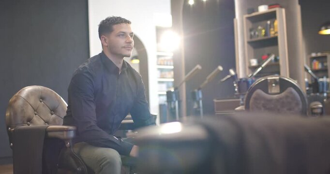 African American man sitting in barber chair in barbershop backlight rising meeting gaze smiling